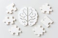 White puzzle pieces surrounding a white paper brain on a white background Royalty Free Stock Photo