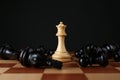 White queen among fallen black chess pieces on wooden board against dark background Royalty Free Stock Photo