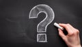 White question mark symbol drawn with chalk isolated over black. Hand holding chalk. FAQ and QA Royalty Free Stock Photo