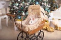 A white rabbit sits inside a retro baby stroller for dolls. Christmas decor, Christmas tree with lights garlands. New Year.