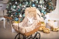 A white rabbit sits inside a retro baby stroller for dolls. Christmas decor, Christmas tree with lights garlands. New Year.