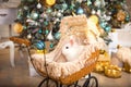 A white rabbit sits inside a retro baby stroller for dolls. Christmas vintage decor, Christmas tree with lights garlands. New Year