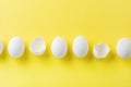 White raw chicken eggs lying in horizontal row with broken egg on yellow background. Top view Royalty Free Stock Photo