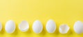 White raw chicken eggs lying in horizontal row with broken egg on yellow background. Top view Royalty Free Stock Photo