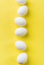 White raw chicken eggs lying in vertical row with broken egg on yellow background. Royalty Free Stock Photo