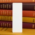 white rectangular bookmark standing upright with soft shadows against blurred stack of yellow orange and red books in warm indoor Royalty Free Stock Photo
