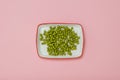 White rectangular plate with green peas on a pink background. Royalty Free Stock Photo