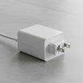 A white, rectangular power adapter with a three-prong plug is lying on a light gray Royalty Free Stock Photo