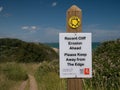 A white rectangular sign fixed to a wooden post next to a path warns walkers of recent cliff erosion on the coast path.