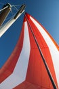 White-red developing sail on a yacht mast against the blue sky, bottom view. Traveling by sea on sunny day. Leisure Royalty Free Stock Photo
