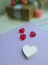 White and red hearts in front of gift box on lavender paper background.
