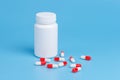 White and red pills, tablets and white bottle on blue background. Royalty Free Stock Photo