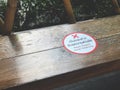 The white and red sticker labeled `Please respect social distancing` is placed on a long bench in the park.