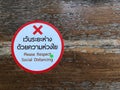 The white and red sticker labeled `Please respect social distancing` is placed on a long bench in the park.