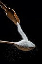 White refined sugar crystals falling down into the wooden spoon at black background
