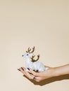 White reindeer Christmas ornament in a woman`s hand isolated on beige background. Creative New Year and Xmas celebration Royalty Free Stock Photo