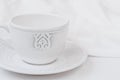 White relief ceramic tea cup with saucer on wood table cotton fabric, purity concept, minimalist