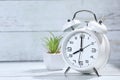 White retro alarm clock on the wooden table. Green plant in a white pot.