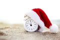 White retro clock alarm with red santa hat standing in the sand. first day of the new year. new year`s morning on the beach. Happ Royalty Free Stock Photo