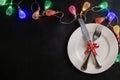 White plate with knife and fork tied with red festive ribbon. Garland of colorful lights. Place for text
