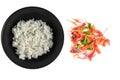 White rice in black matte plate and colorful chopped fresh vegetables mix isolated on a white background, top view
