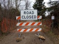 White road closed sign and striped barricade with trail or path