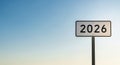 A white road sign displaying the year 2026 stands against a clear blue sky with a soft gradient of light Royalty Free Stock Photo