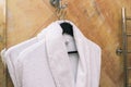 White robe in the bathroom. The hotel room`s Terry-cloth robe hangs on a hanger near the marble wall. Concept of leisure Royalty Free Stock Photo