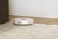 White robotic vacuum cleaner on a carpet cleaning dust in living room interior. Smart electronic housekeeping technology. Shallow Royalty Free Stock Photo