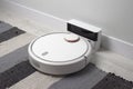 White robotic vacuum cleaner charging on white and black carpet in the living room. Smart electronic housekeeping technology