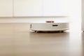 White robotic vacuum cleaner on laminate floor cleaning dust in living room interior. Smart electronic housekeeping technology. Royalty Free Stock Photo