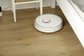 White robotic vacuum cleaner on laminate floor cleaning dust in living room interior. Smart electronic housekeeping technology. Royalty Free Stock Photo