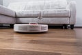 White robotic vacuum cleaner runs on the laminate floor Closeup. The robot is controlled by voice commands for direct cleaning.