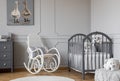 White rocking chair with pillow next to wooden cradle in elegant baby room with duck`s poster on the wall Royalty Free Stock Photo