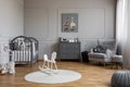 White rocking horse on rug in grey baby`s bedroom interior with poster above cabinet. Real photo Royalty Free Stock Photo