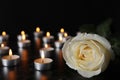 White rose and blurred burning candles on table in darkness, closeup. Funeral symbol Royalty Free Stock Photo