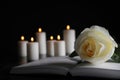 White rose, book and blurred candles on table in darkness, closeup with space for text. Funeral symbol