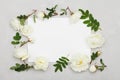 White rose flowers, green leaves and clean paper sheet on light gray background from above, beautiful floral pattern, flat lay