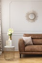 White roses in a vase on the stylish table next to brown leather sofa in light living room