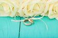 White roses and wedding rings on blue wooden background. Selective focus