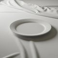 A white, round ceramic plate rests on a draped white tablecloth, creating subtle shadow Royalty Free Stock Photo