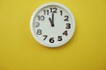 White round clock showing eleven o`clock on yellow background