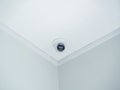 A white round indoor CCTV surveillance camera monitoring security on ceiling in the room corner inside the white clean building. Royalty Free Stock Photo