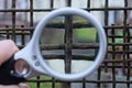 A white round magnifier in the hand magnifies the brown rusty iron grate