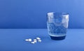 White round medical pills, vitamins, in the distance there is a beautiful blue glass with clean water.