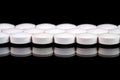 White round pharmaceutical pills on reflective surface, black background