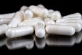 White oblong pharmaceutical capsules on reflective surface, black background Royalty Free Stock Photo