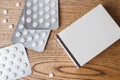 White round pills in aluminum packaging and white box of pills on a wooden table, copy space