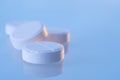 White round pills on a blue mirror surface with copy space, close up. Medicines on glass lit by the morning sun