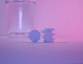 White round pills cost pyramid. One pill stands on the rib next to it. In the background a glass of water.  Pink light. The concep Royalty Free Stock Photo